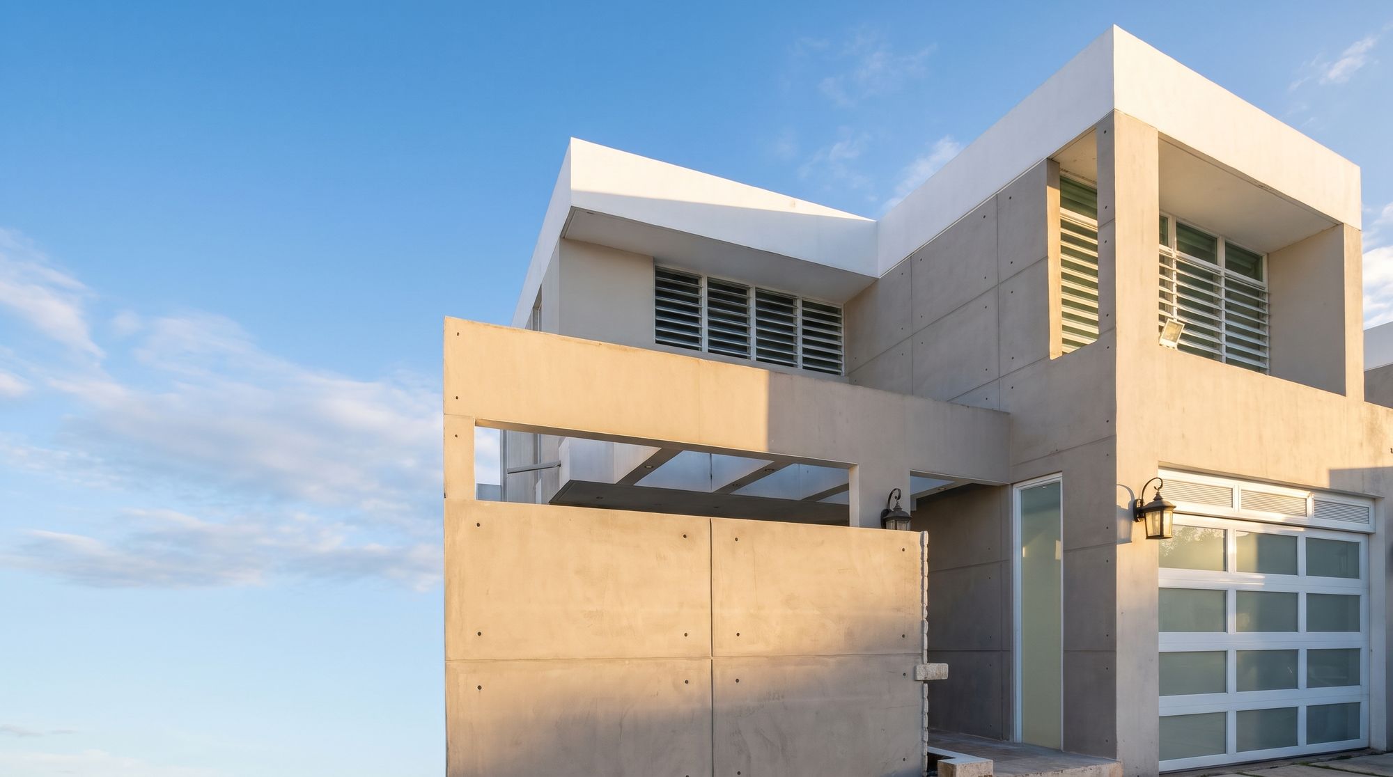 Fachada contemporánea de la residencia en Vega Dorada, con hormigón expuesto y portón de cristal